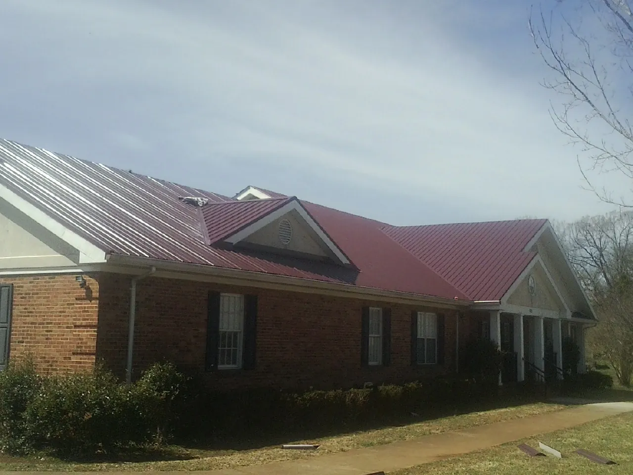 Red metal roof with gabled entries on a long brick building, from a Hail Damage Roof Repair job in Sunbury