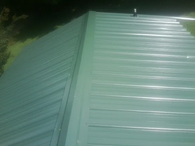 New green metal panels meeting at the ridge of a roof — Flat Roof Repair work by our crew in Sunbury